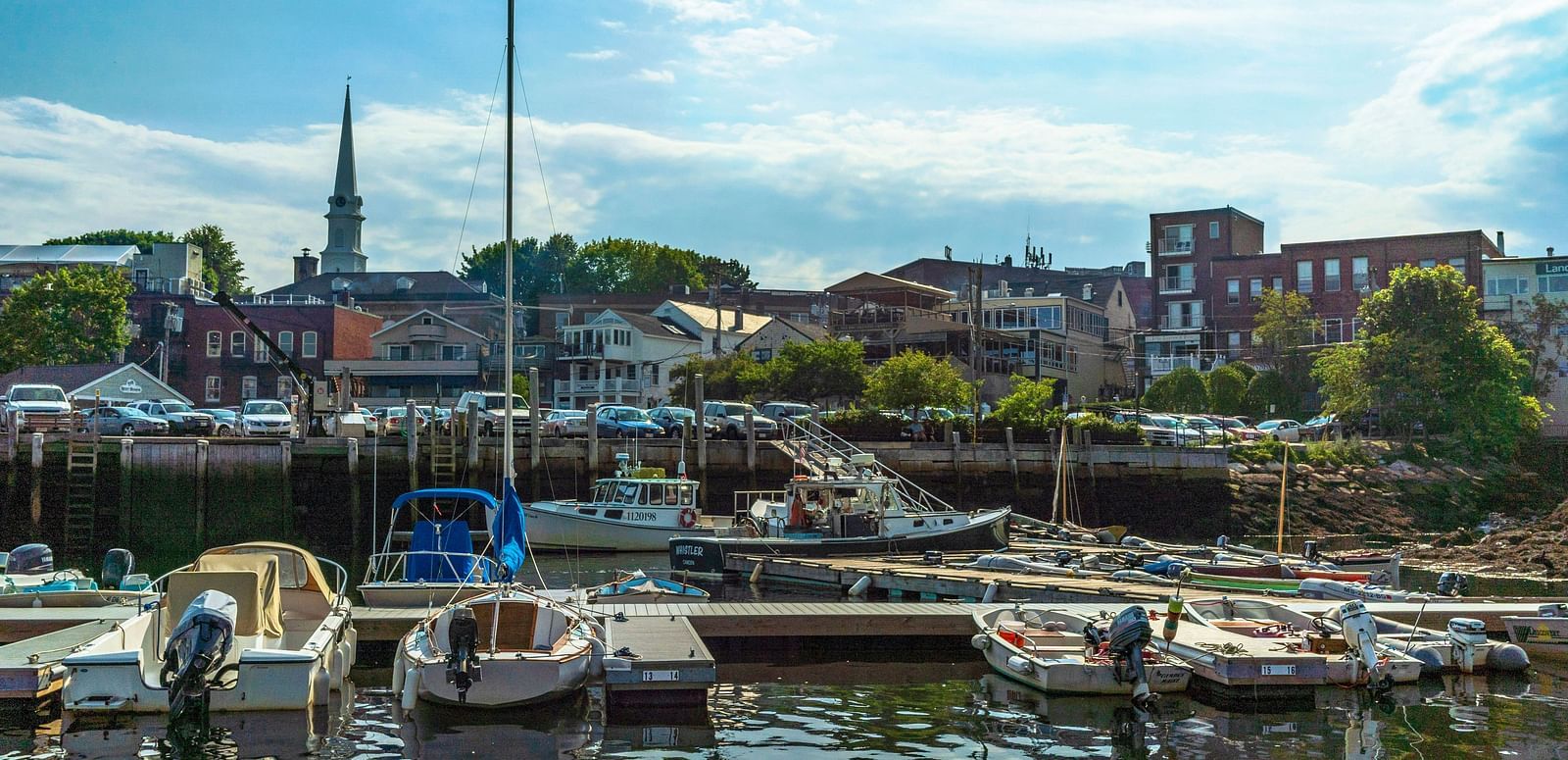 Small boats docked at a harbour with buildings and trees in the background.