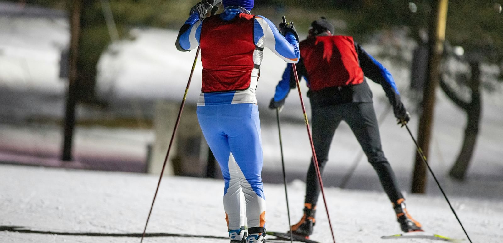 Two people cross-country skiing on a snow-covered trail.