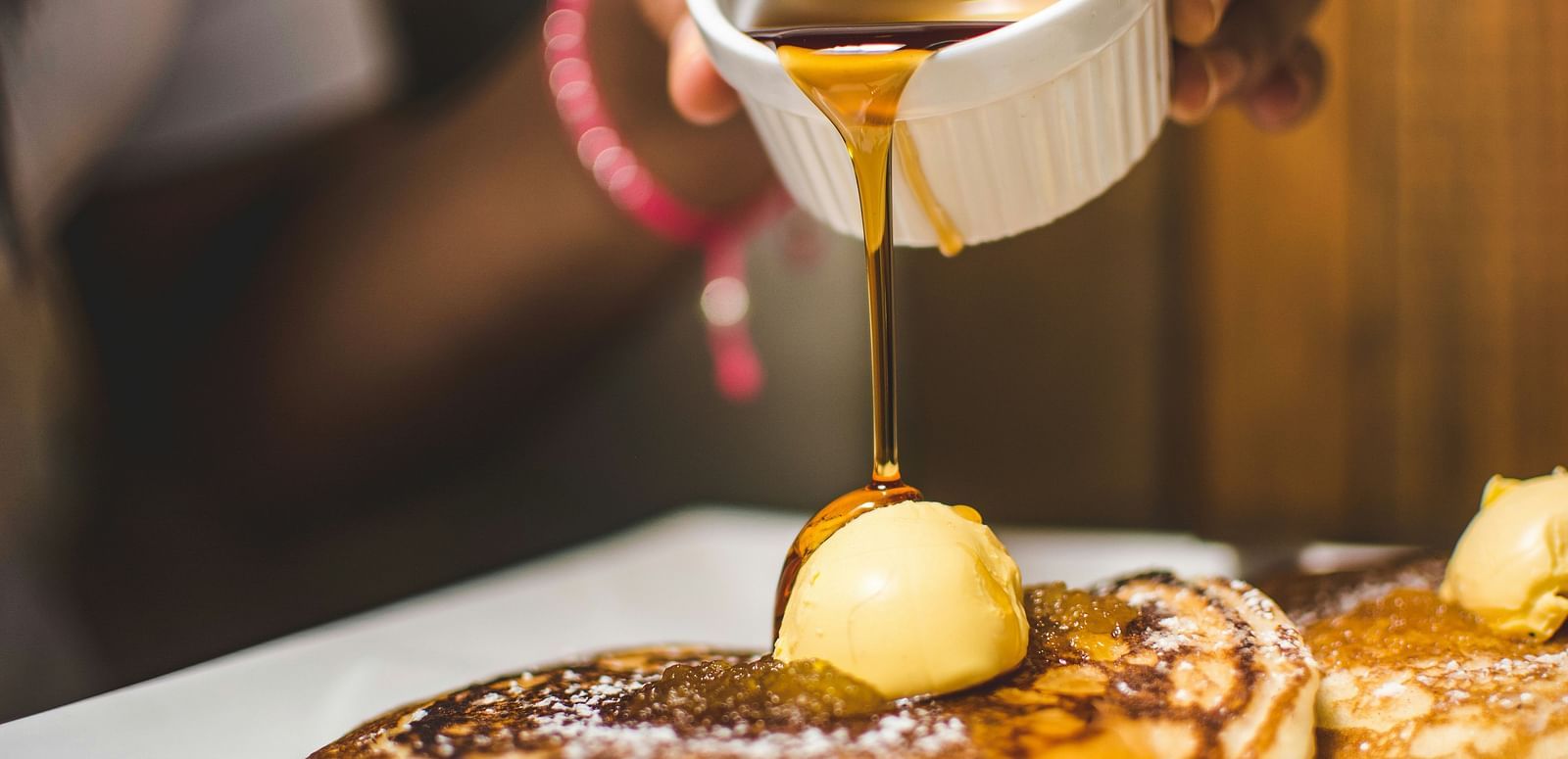 Syrup being poured over a stack of fluffy pastries.