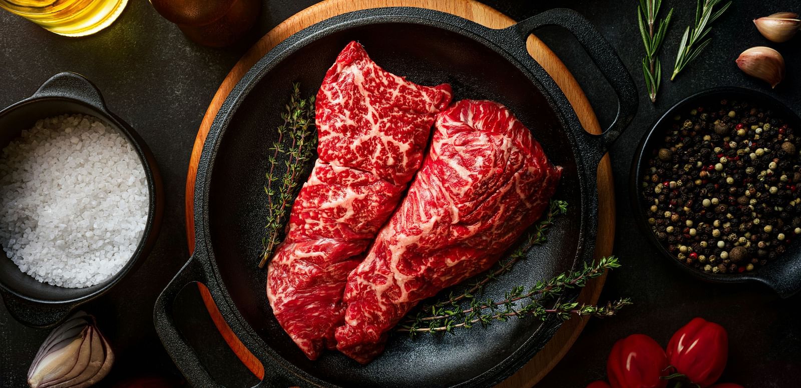 A raw steak on a skillet surrounded by spices, herbs, and vegetables.