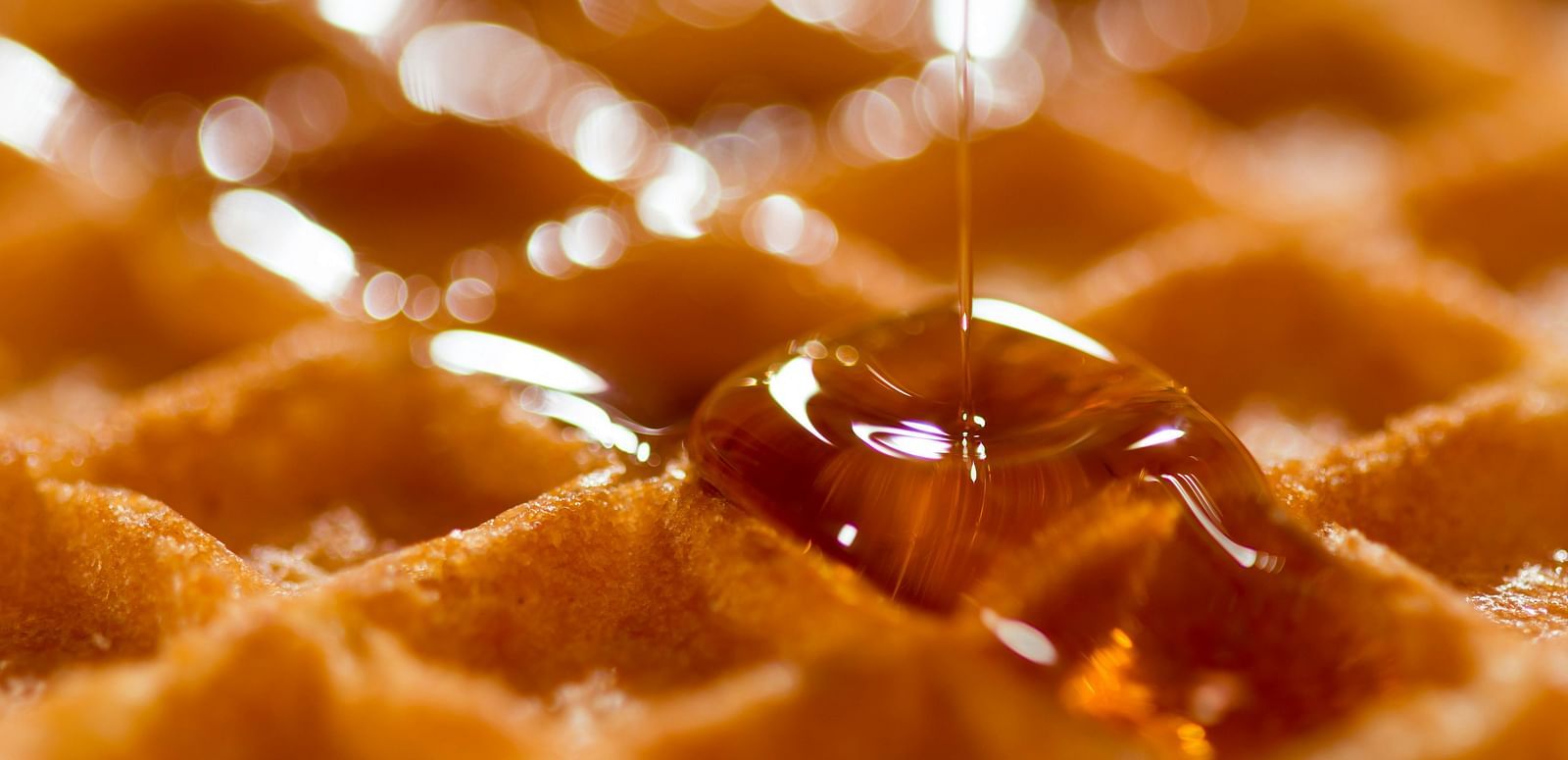 A close-up shot of honey being poured on a waffle.