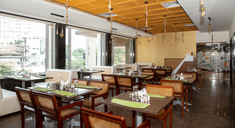 Seating area in the dining hall featuring large windows, multiple tables, and wooden chairs, at Icon Express By Bhagini, Mahadevapura.