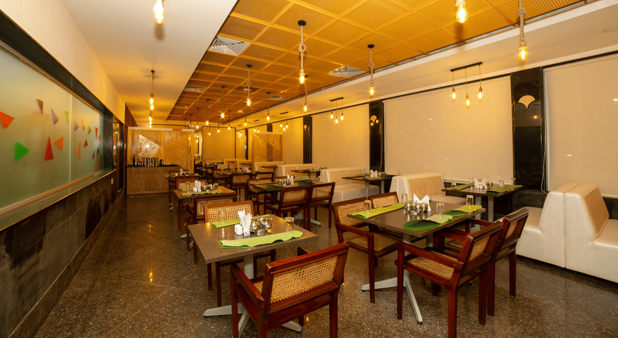 Wide view of the main dining hall, showing arranged tables, chairs, white booths, and a decorative ceiling at Icon Express By Bhagini, Mahadevapura.