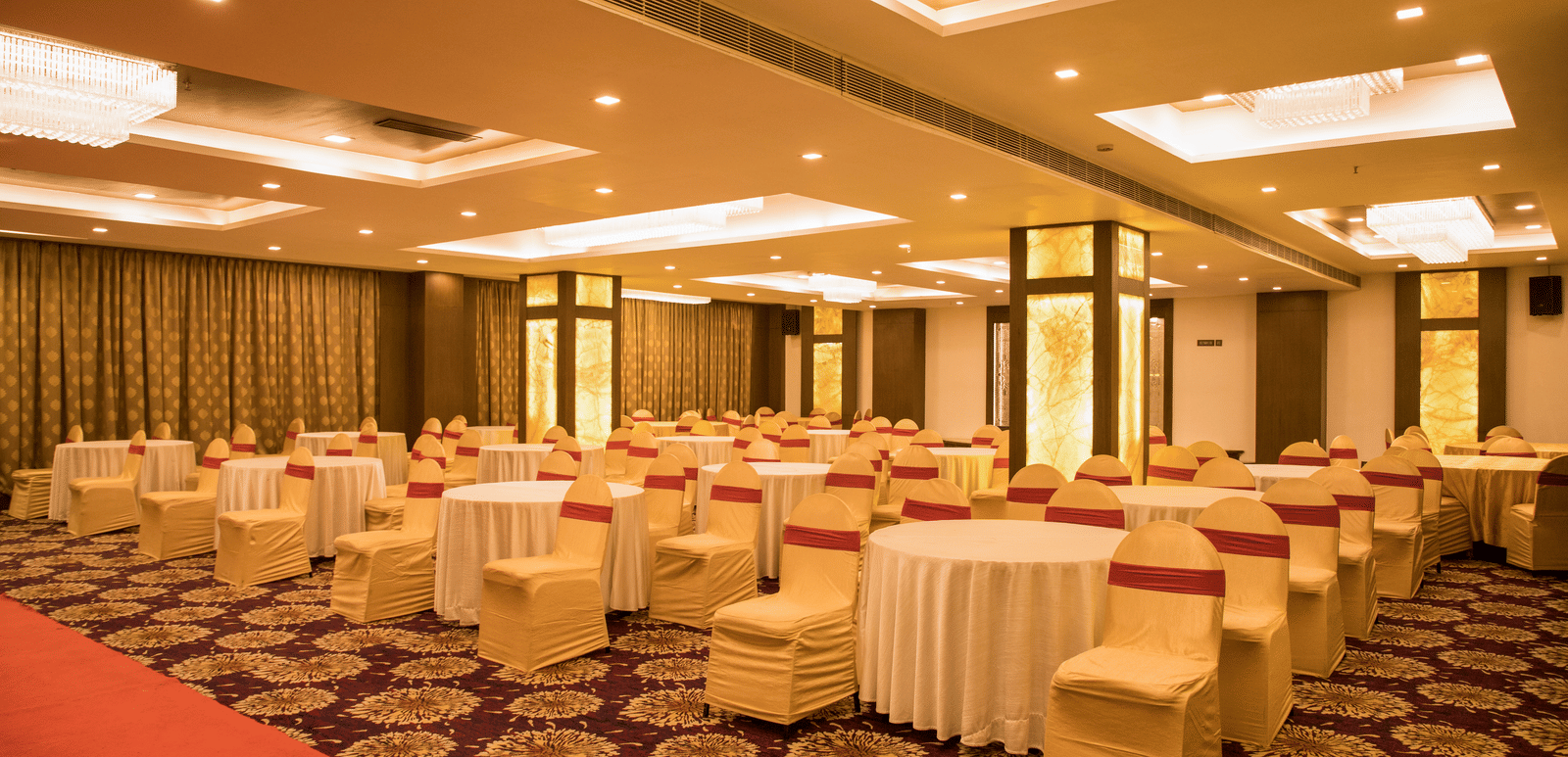 A spacious banquet hall at Benzz Park Chennai with numerous round tables draped in white, set for a gathering.