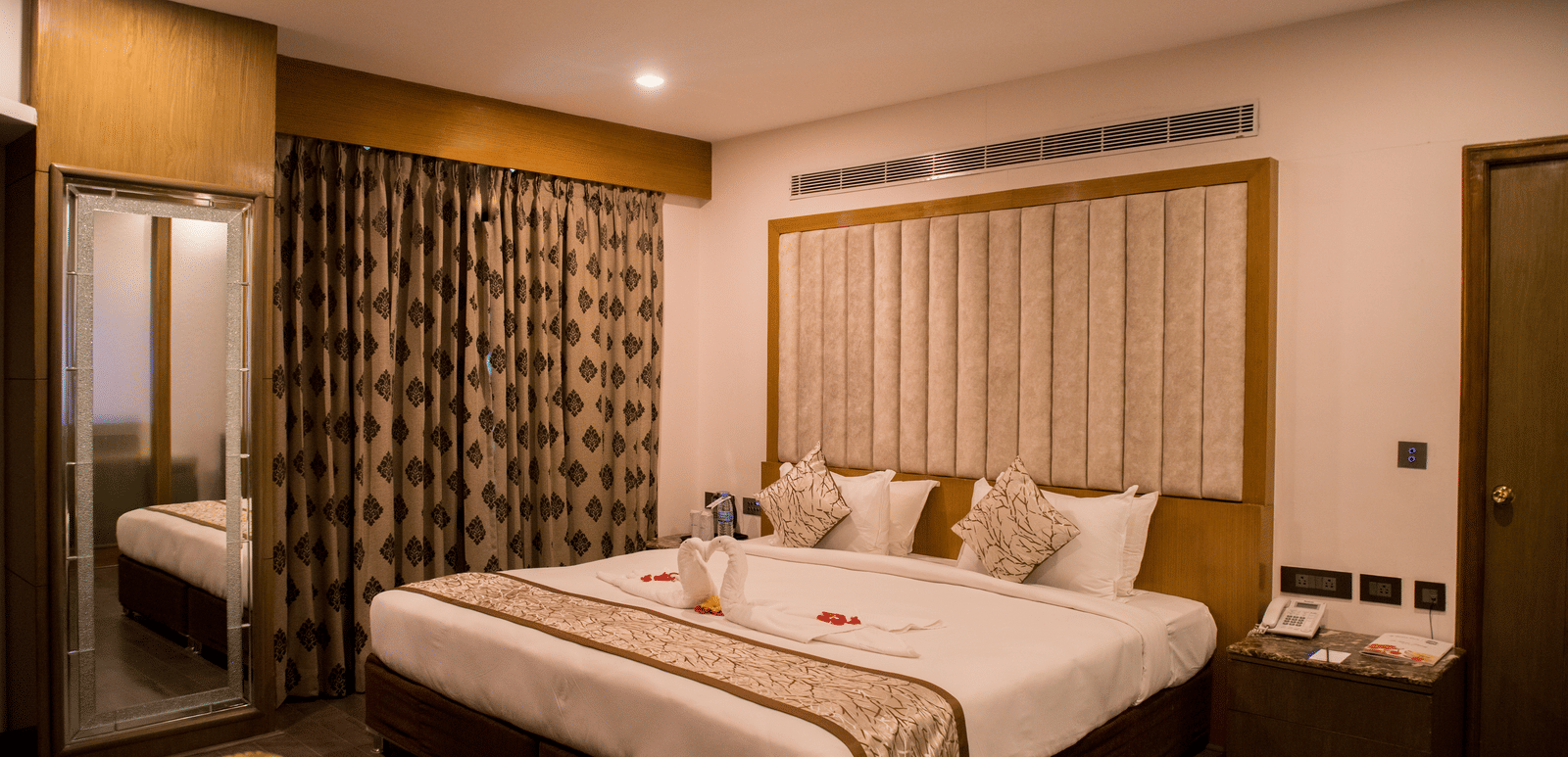 A hotel room at Benzz Park Chennai featuring a neatly made bed with white linens, a bedside table, and curtains.