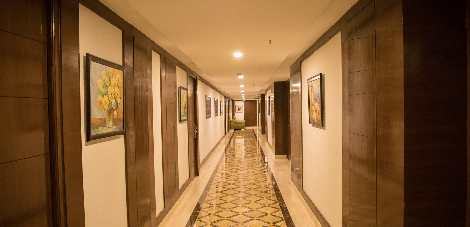A long, well-lit corridor in Benzz Park Chennai with patterned wallpaper and framed artwork, leading to guest rooms.