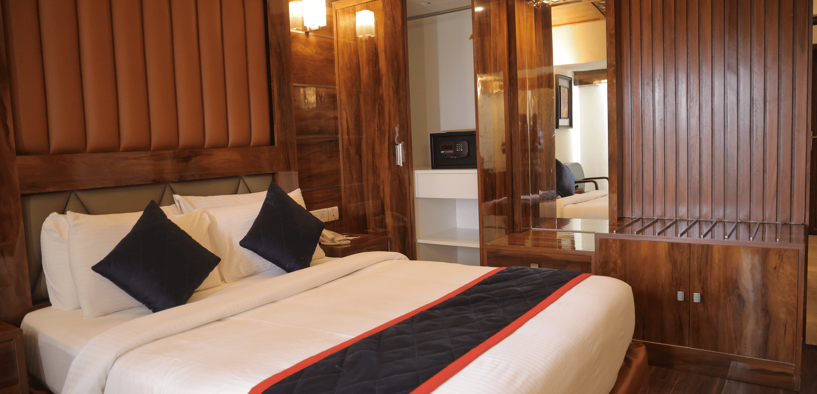 A spacious hotel suite with a large double bed, wooden panelling, and mirrored wardrobe doors - Benzz Park, Kodaikanal
