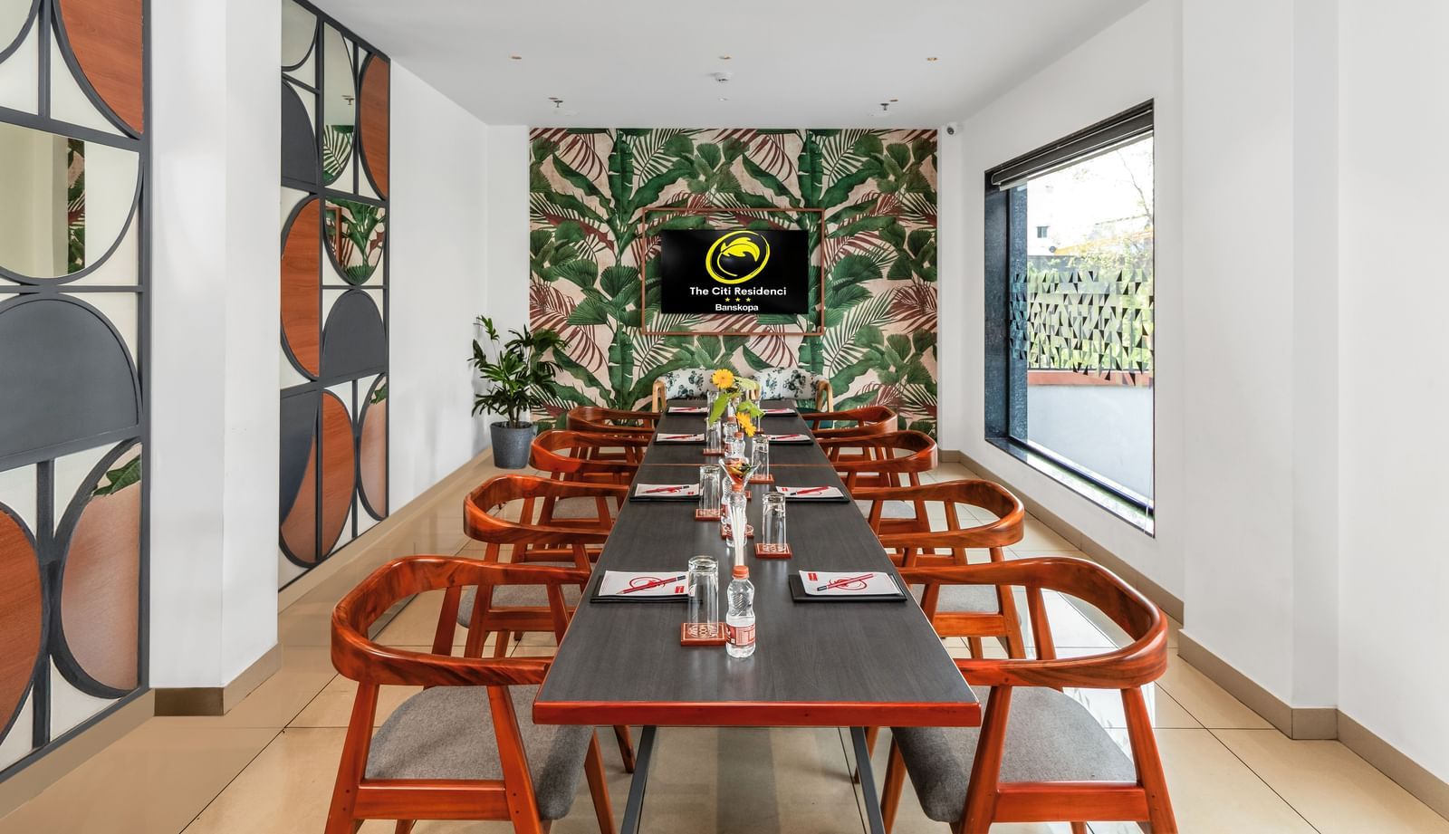 A modern meeting room with a long table, wooden chairs, a tropical-themed wallpaper, and a wall-mounted screen | The Citi Residenci Hotel Banskopa
