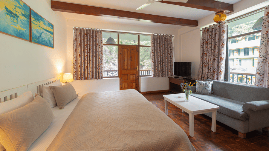 A cottage-style bedroom featuring exposed ceiling beams, a grey sofa, and a white coffee table - Johnson Lodge & Spa, Manali
