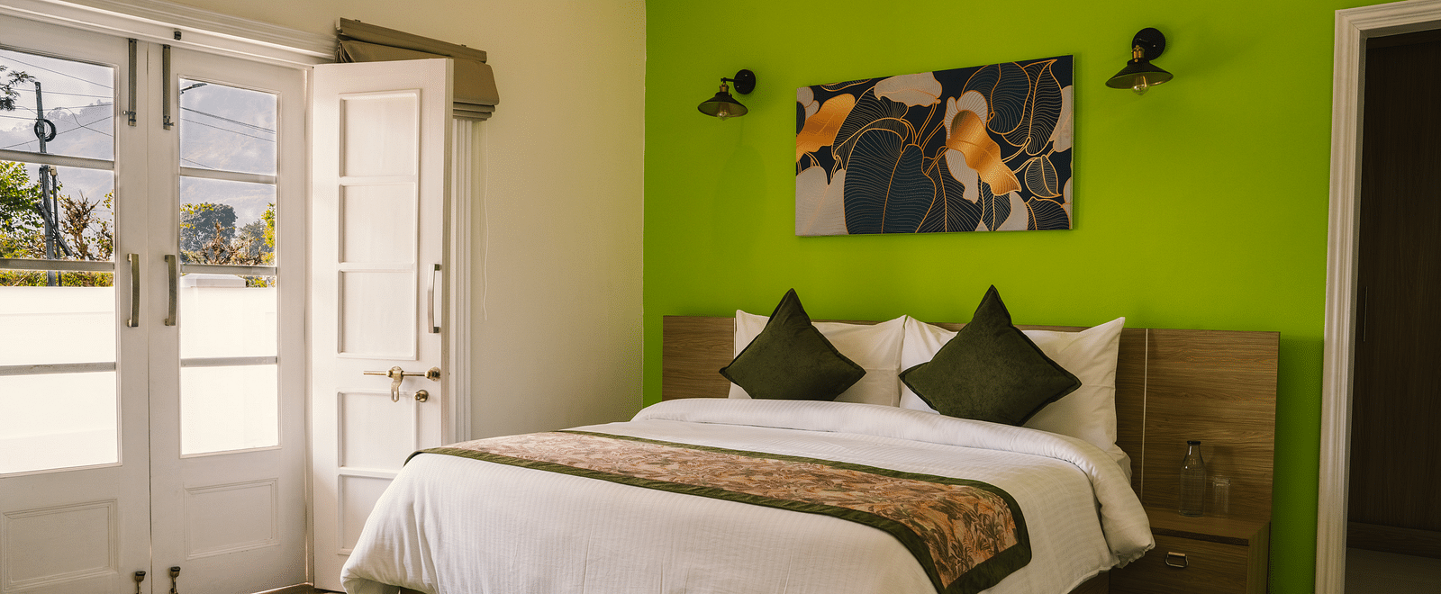 A spacious room at BluSalzz Villas - The Green Roof, Bhimtal featuring a large bed, a photo frame above the headboard, a carpet, and a door leading to the balcony.