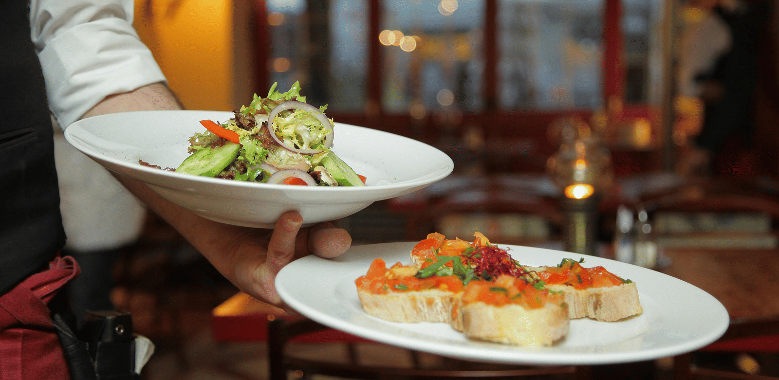 a person in a restaurant holding two plates with delicious cuisines in it that are well plated