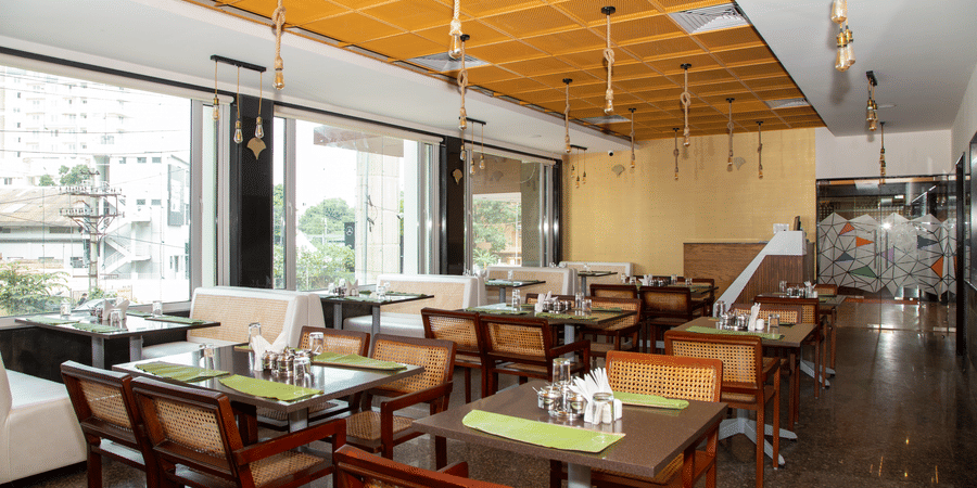 Seating area in the dining hall featuring large windows, multiple tables, and wooden chairs, at Icon Express By Bhagini, Mahadevapura.