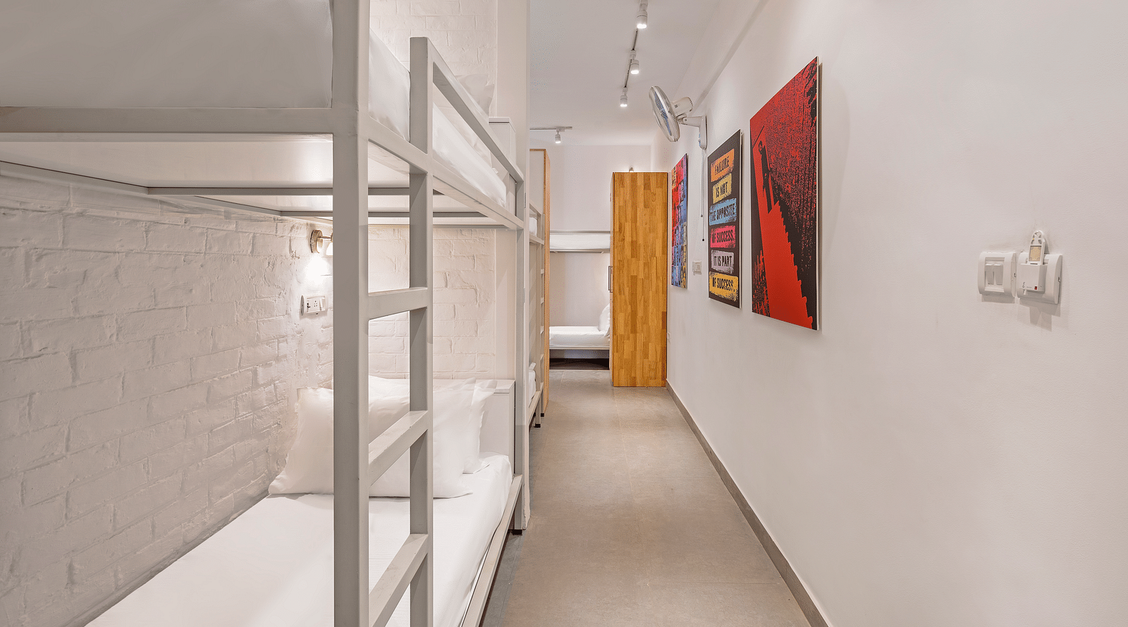 An image of dorms with the bunker beds, in bedzzz Varanasi, with few painting hanging on the wall, lighting and cupboard in it. 