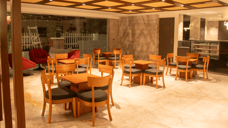 A hotel lobby area with wooden tables and chairs,  cushioned chairs, and ceiling lights arranged in a grid pattern.