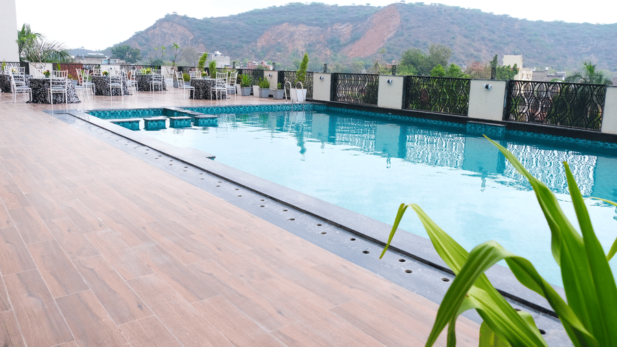a rooftop infinity pool bordered by a wooden deck, with a mountain in the background | Pride Premier Alwar