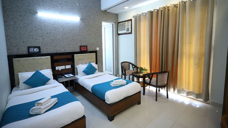 A room with two single beds with blue accents, wooden furniture, and curtains covering the window - Asian Suites Cyber Park, Gurgaon