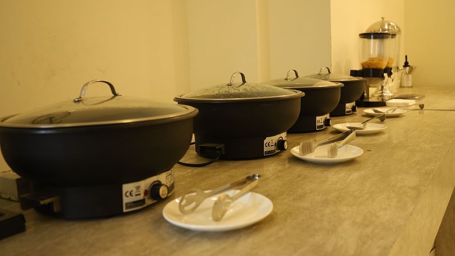 A close-up of a buffet setup shows large black serving dishes and various food items on a counter - Asian Suites Cyber Park, Gurgaon