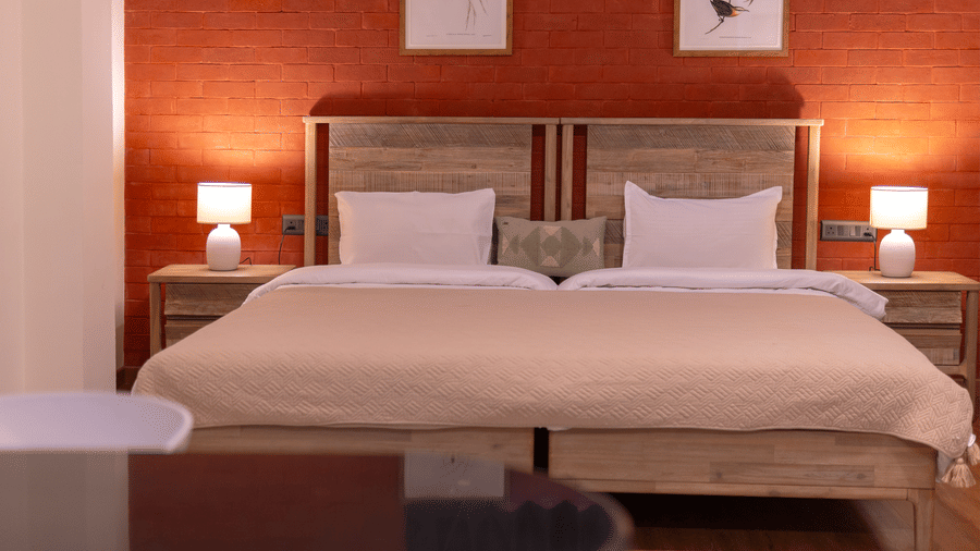 Close-up of twin beds with white linens and bedside lamps set against a textured rustic orange wall - Johnson Lodge & Spa, Manali