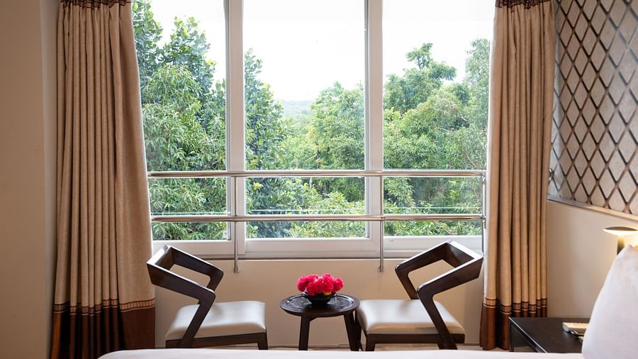 Image of two chairs and a small centre table by the window overlooking the lush green lawn | The Grand Legacy Resort and Spa