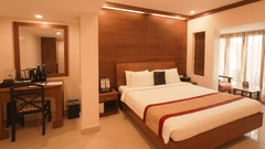 A room with a neatly arranged bed with good lighting and a desk and chair arranged in the side.