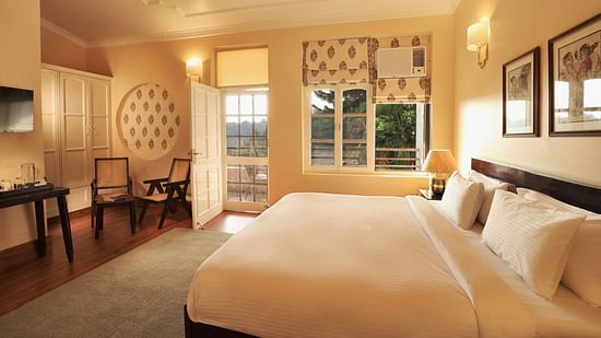 An image of a Super Deluxe Room featuring a double size bed, two chairs, a table where coffee maker is kept, and an open door from where sunlight is flooding the room - Lamrin Boutique Cottages Rishikesh