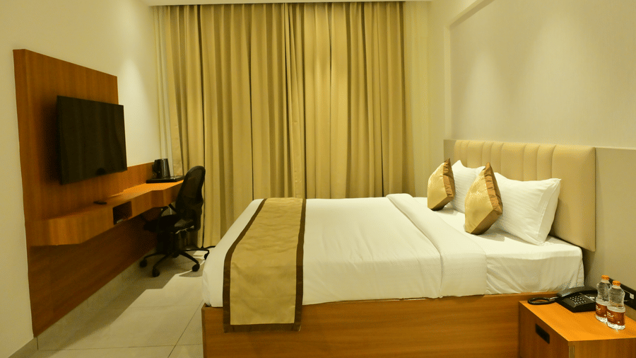 Deluxe room at Bhavanis Vista By Icon Hosur with a king bed, wooden work desk, and gold-toned curtains.