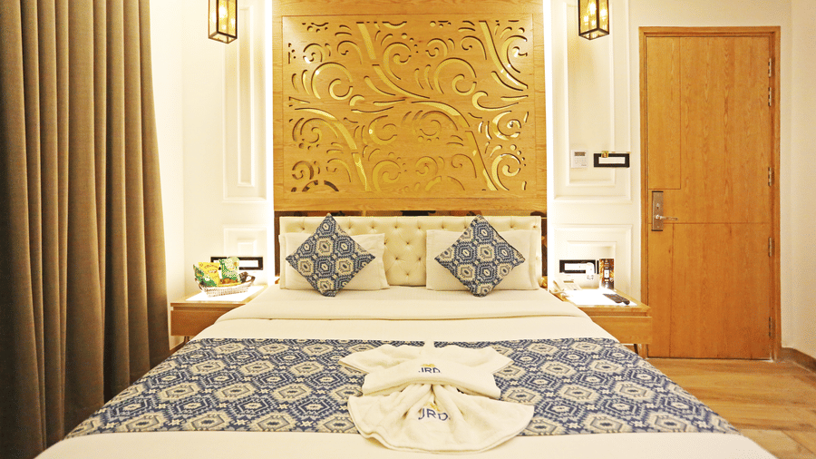 A bedroom featuring a neatly-made bed with blue-patterned cushions and an ornate wooden headboard at JRD Luxury - Business Hotel.