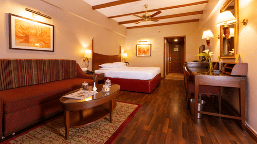A bedroom at The Carlton in Kodaikanal featuring a double size bed, a work desk and chair, TV screen, a sofa and centre table.