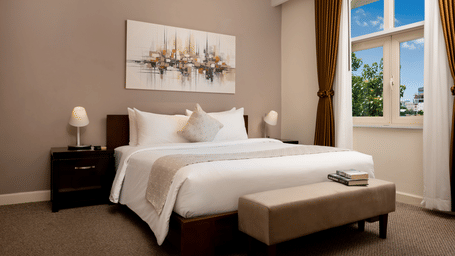 One Bedroom Suite bedroom at Central Mansions, Phnom Penh featuring a king bed, bedside tables, upholstered bench, and arched windows.