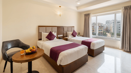 A Superior Twin Room at Destino by Monday Hotels, Gachibowli, with twin beds, a small table with a fruit basket, and a modern chair.