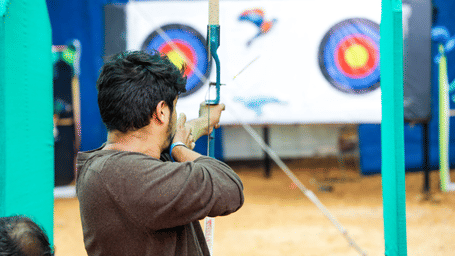 A man aims his bow towards a large archery target on an outdoor range - District Gravity Adventure Park, Hyderabad