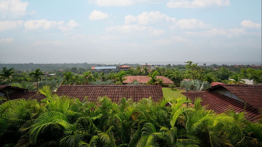 A panoramic view of lush greenery with traditional red rooftiles peeking out from the dense canopy, captured on a cloudy day - Crescent Resort, Goa