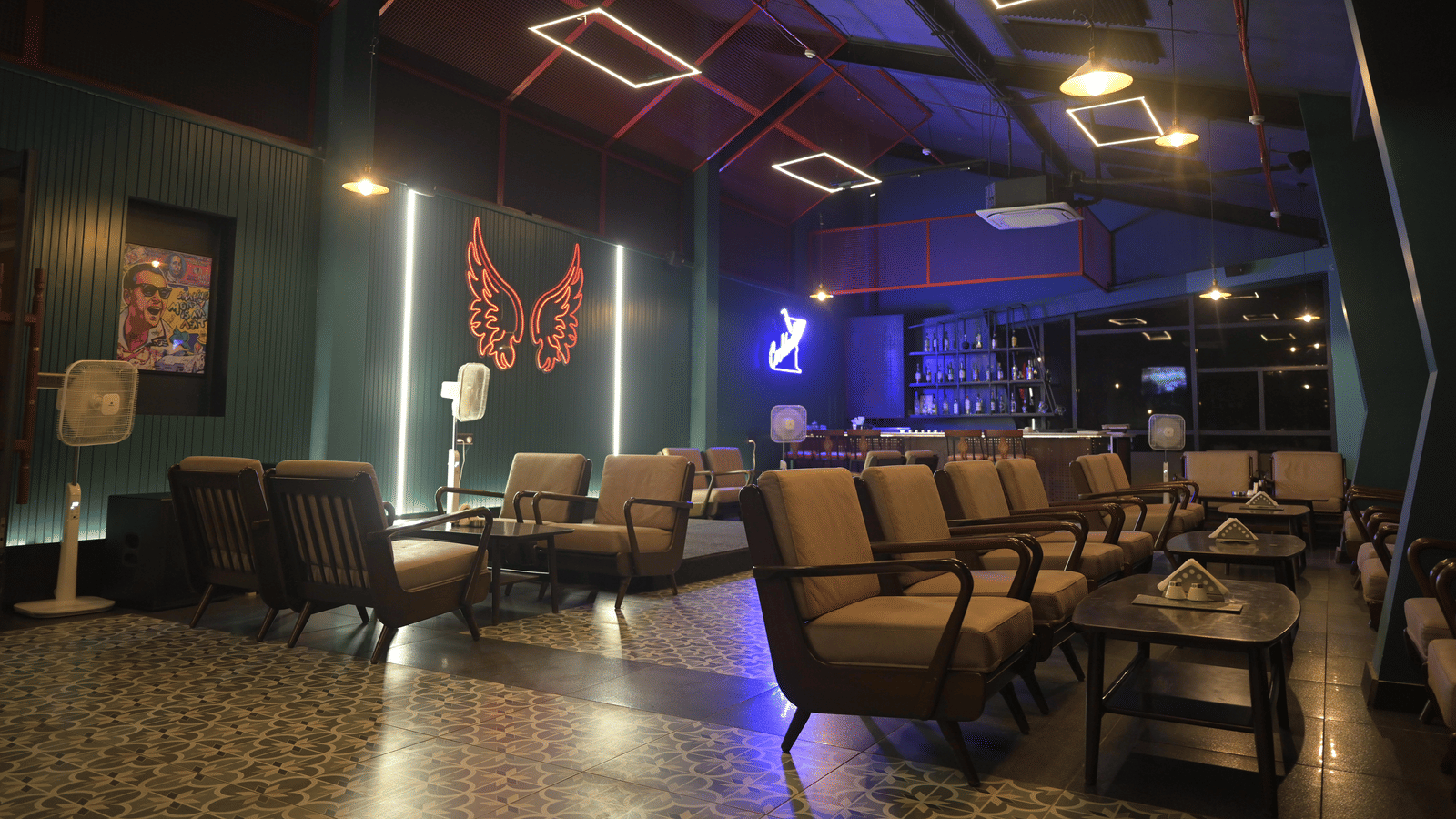 A cosy lounge setting featuring cushioned chairs and a neon butterfly wall installation glowing in the background at Hotel Sonar Bangla Mayapur.