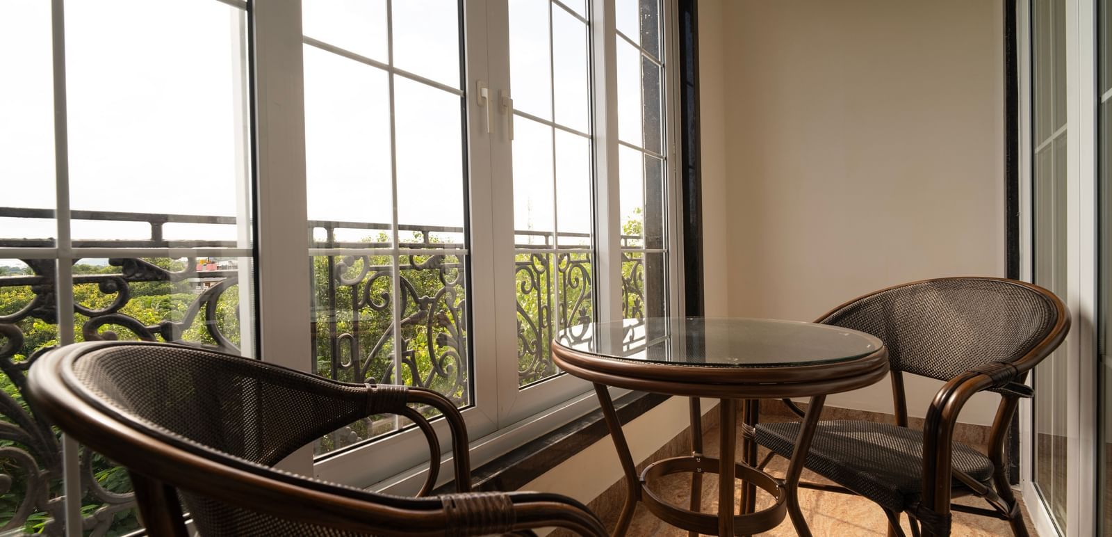 A balcony with dual seating arrangement with a coffee table and sun light filtering through french windows - Accord Chrome Airport Hotel