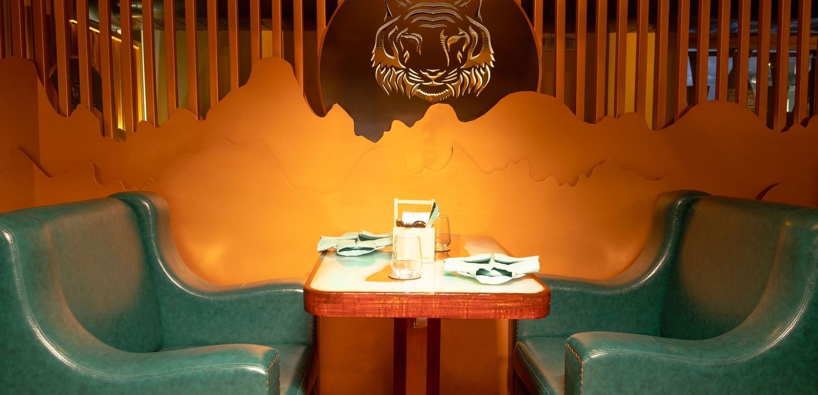 A stylish booth seating area with green chairs and a golden wall decor - Accord Puducherry