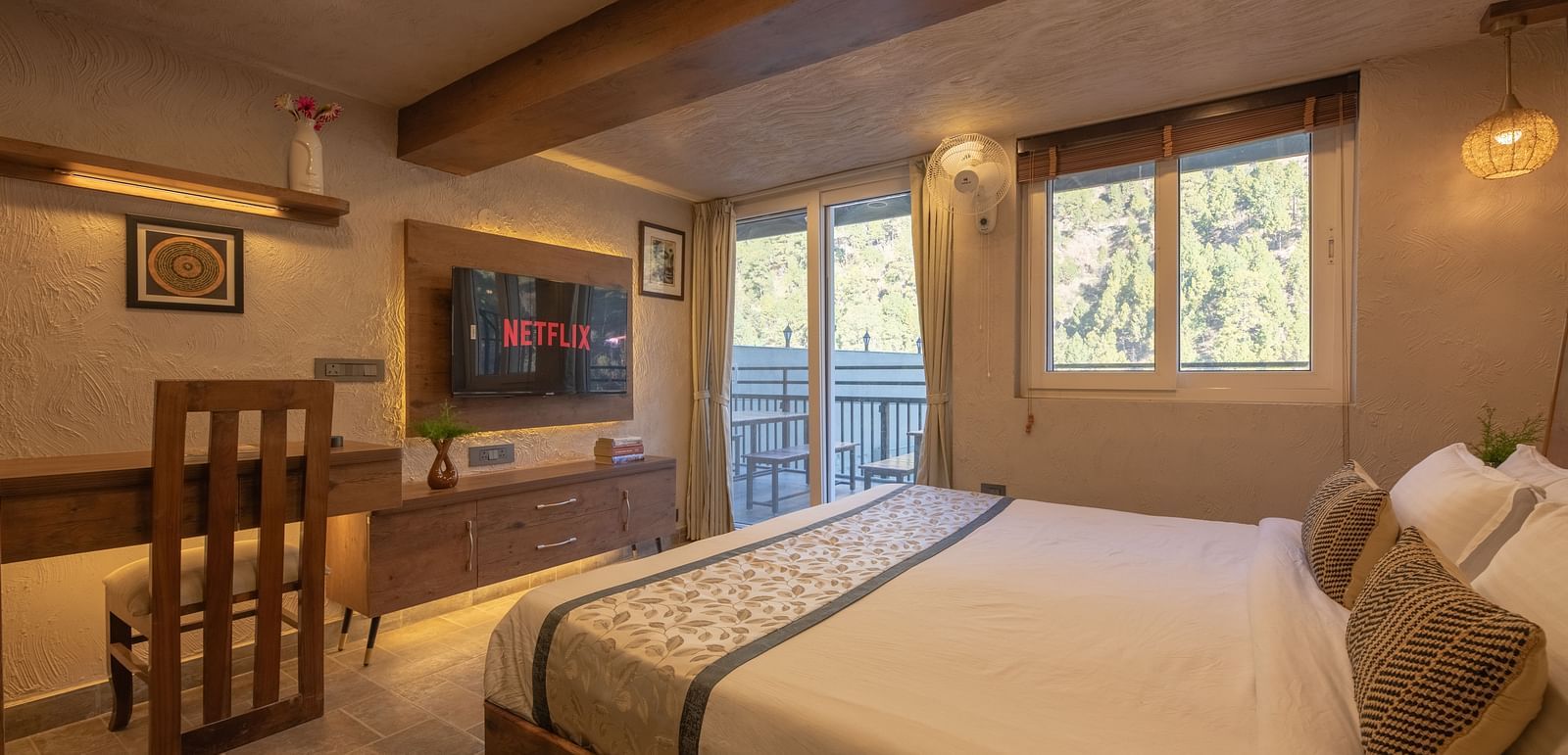 Room with double bed, TV, balcony doors, wooden beams on the ceiling, and soft lighting.