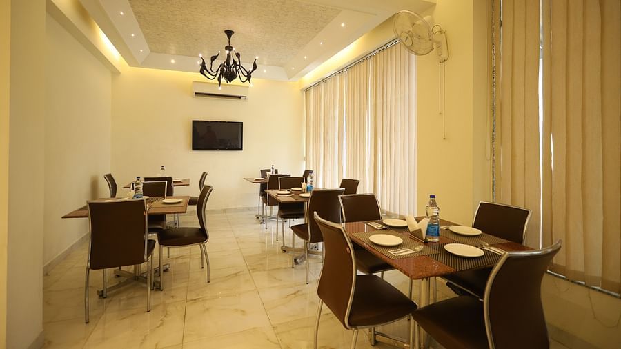 A well-lit dining space with several tables and chairs is decorated with sheer curtains and a chandelier - Asian Suites Cyber Park, Gurgaon