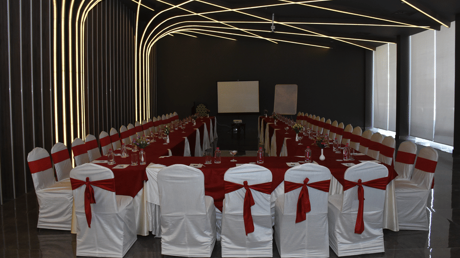 A banquet hall at Comfort Inn Sapphire by Eastlynn Collections, Jaipur with arranged chairs, table, stage area, and decorative wall lighting.