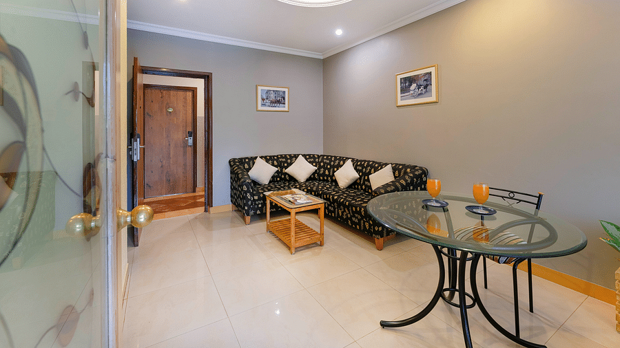 A seating area in our Suite in Bangalore with a glass table, a chair and a comfortable couch - Cross Roads Inn, Bengaluru