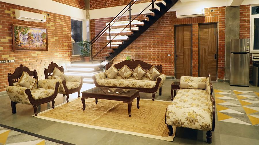 A living area featuring a modern sofa set with a sleek staircase in the background at Tisya Farms, Gurgaon.