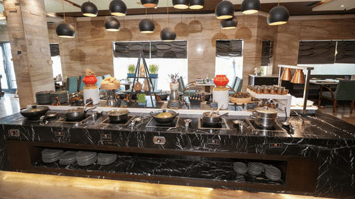 A buffet counter at Park Plaza Ludhiana featuring a dark marble surface with food displays hanging pendant lights and a stone textured wall backdrop in a warmly lit setting.