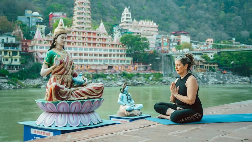 elderly woman meditating in front of a statue of Parvati on the Ganges