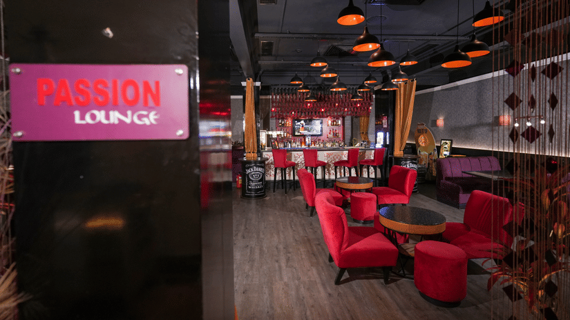Interior of Passion Lounge at Park Plaza Ludhiana featuring red upholstered seating dark wooden flooring a glowing pink neon sign and warm ambient ceiling lighting.
