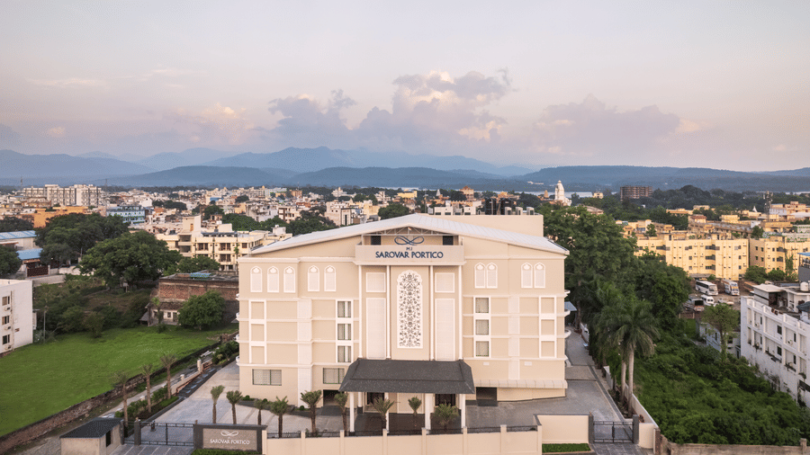 A facade image of MJ Sarovar Portico with a backdrop of city and mountain views - MJ Sarovar Portico, Haridwar