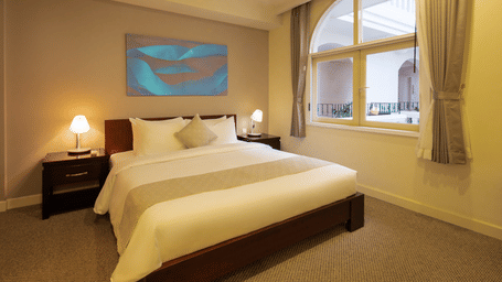 Two Bedroom Family Suite bedroom at Central Mansions, Phnom Penh with a king bed, bedside tables, and arched windows.