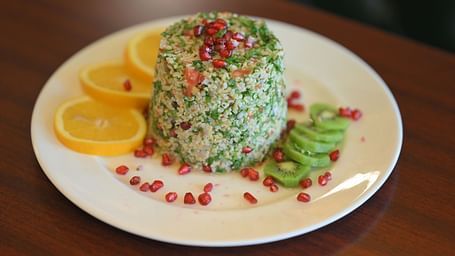 A fresh and healthy bulgur salad garnished with pomegranate seeds, lemon, and kiwi at Royal Comfort Regency.