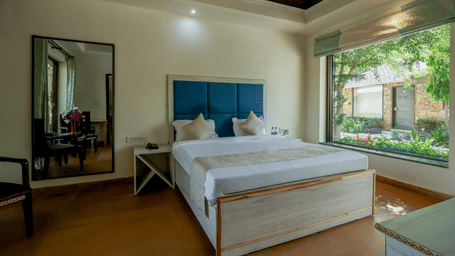 French Deluxe with Garden View room featuring a bed with a blue headboard, tall mirror and large window overlooking greenery at Valley by Grassfield.