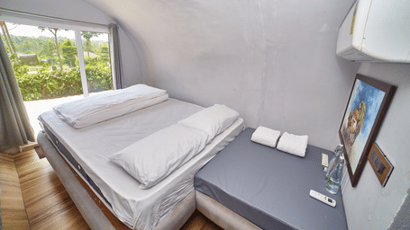 The interior of a modern, capsule-style accommodation unit featuring a single bed with a white mattress and a small bedside table, with a window offering a view of greenery. - Vintage Trails by Ilara