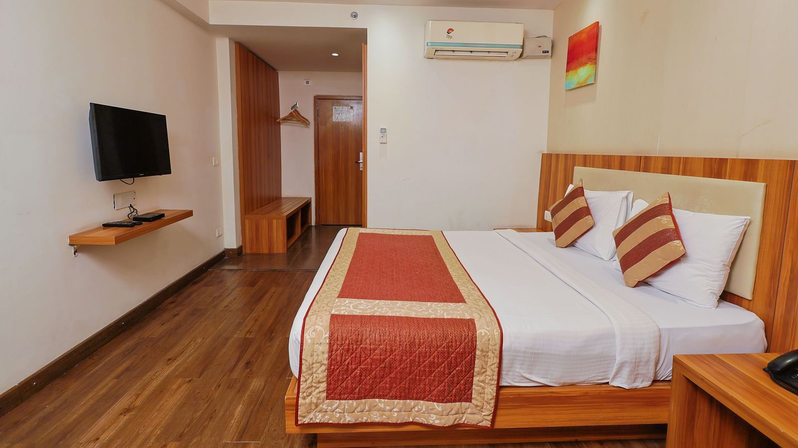 A wide angle side view of the bedroom with plushy bed and TV a small corridor haeding towards to door at Le Roi udaipur