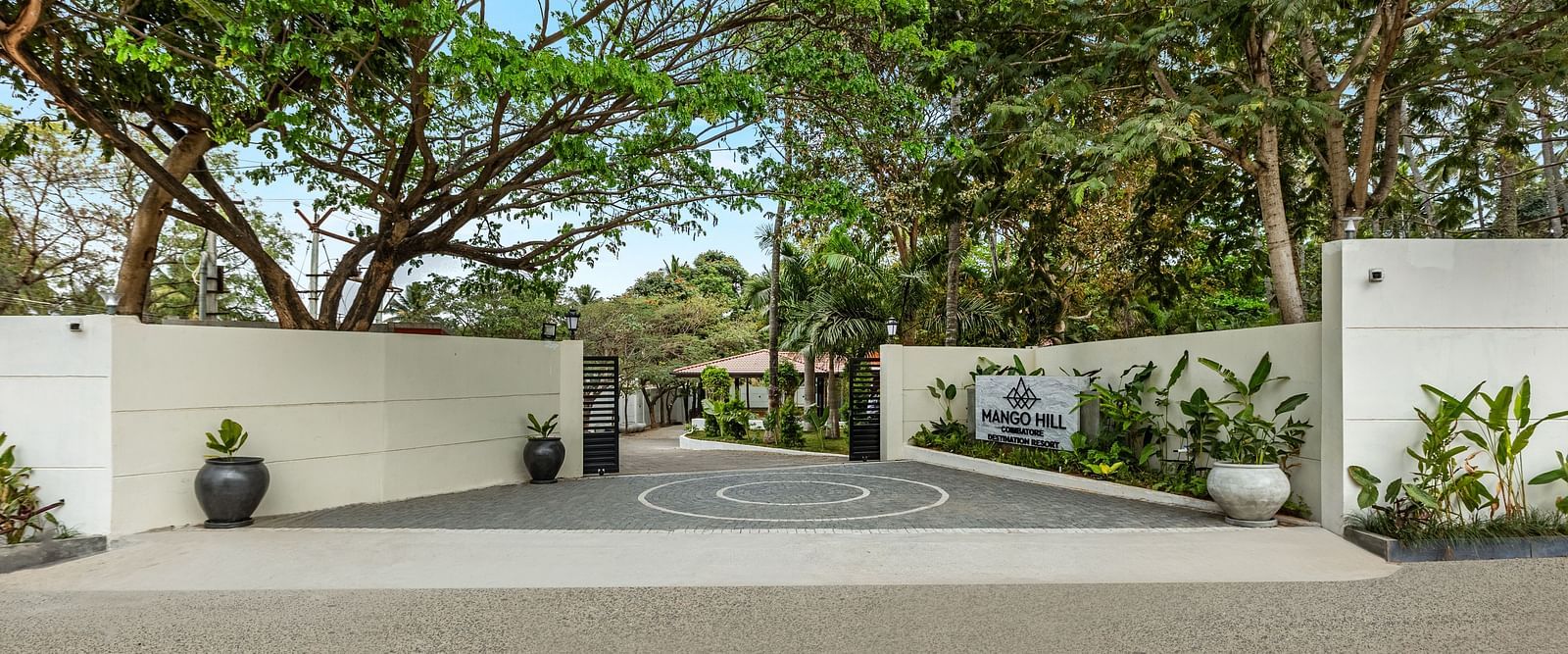 The illuminated entrance to Mango Hill Resort, Coimbatore, featuring a white gate, a sign, and trees at night